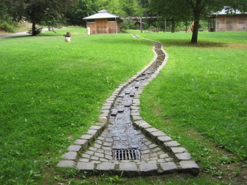 Am Ausgangspunkt des Ökologischen Bachlehrpfads wird gezeigt, wie man nicht mit Bächen umgehen soll: gepflastert aufheizen, versickern, ins Rohr stürzen lassen. - Leider weist auf all dies die Info nicht hin.