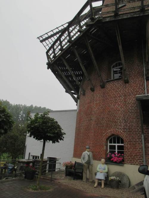 Herr und Frau Müller vor ihrer Doppelmühle, Wasser- und Windmühle an einem Standort.