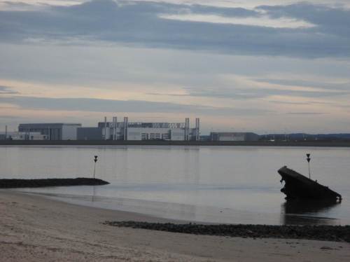 Blick über ein Schiffswrack und das als Elbe-Lunge nicht mehr funktionierende Mühlenberger Loch auf die aufgespülte Airbus-Ansiedlung.